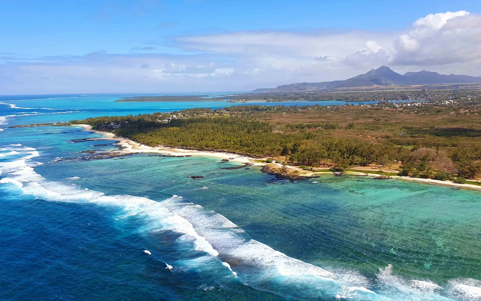 Aerial view of Mauritius’s East Coast, with turquoise lagoon water, a coral reef, white surf and a tree-lined shoreline.